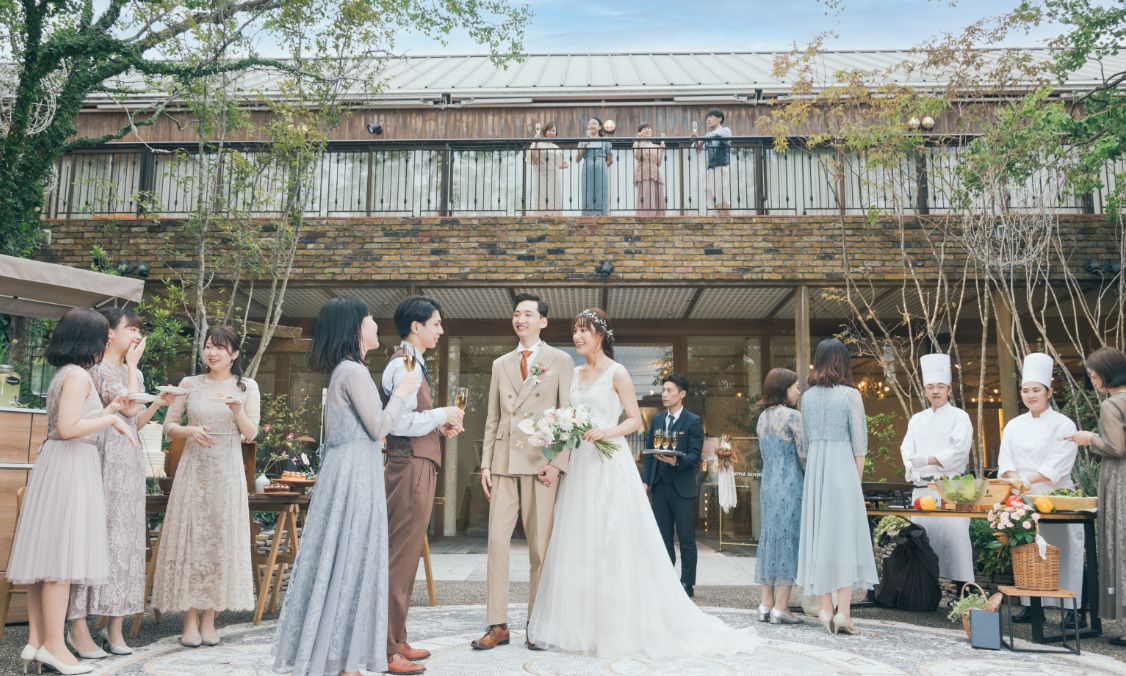 レンガ造りの建物を背景にガーデンパーティを楽しむ新郎新婦とゲスト