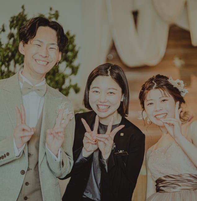 ピースをする笑顔の新郎新婦とプランナー