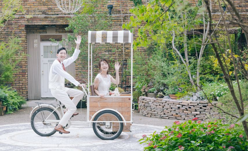オリジナル自転車に乗って笑顔で手をふる新郎新婦