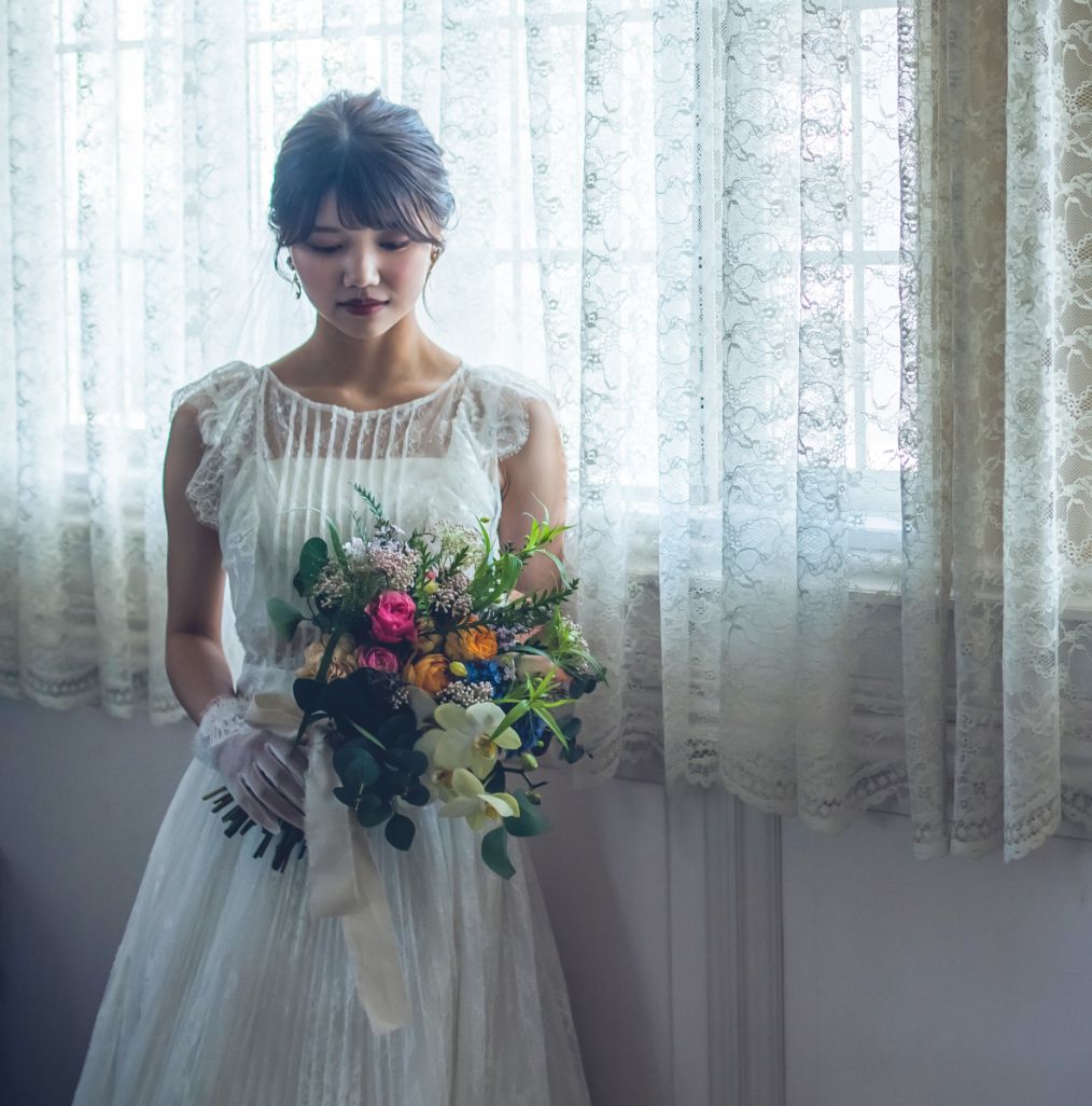 カラフルなブーケを持って窓辺にたつウエディングドレスの花嫁