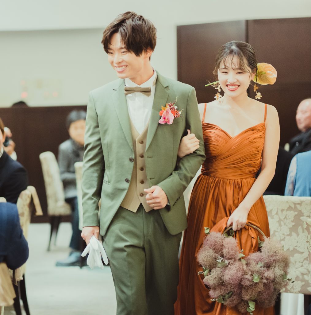 くすみオレンジのカクテルドレスと若草色のスーツの新郎新婦